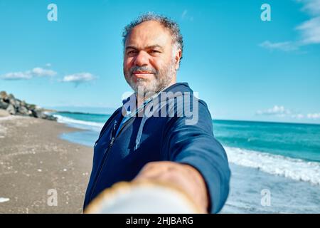 Seguimi. L'uomo tiene e tira la mano del fotografo mentre cammina sulla spiaggia e la conduce verso il mare. Concetto di Unione e moderno spensierato Foto Stock