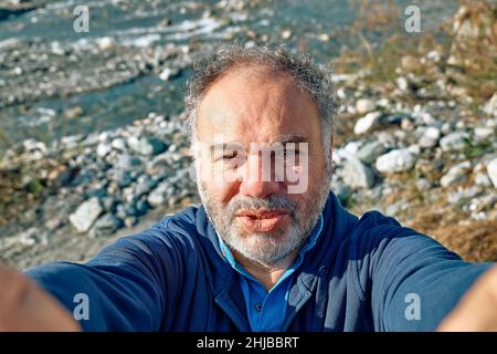 Felice, sorridente uomo maturo barbuto facendo un selfie su sfondo marino. Concetto di attività ricreative, turismo, stile di vita e natura. Foto Stock