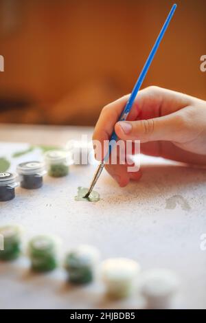 Foto ritagliata sfocata di pittura femminile a mano con pennello su carta, fuoco selettivo su vernici acriliche in scatole di plastica disposte in fila secondo la statura Foto Stock