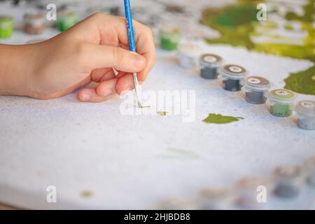 Foto ritagliata sfocata di pittura femminile a mano con pennello su carta, fuoco selettivo su vernici acriliche in scatole di plastica disposte in fila secondo la statura Foto Stock