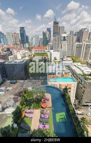 Persone prendere il sole sul tetto dell'hotel con giardino e piscina, edifici alti, Bangkok, Thailandia Foto Stock