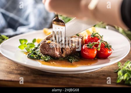 La persona taglia in una bistecca cotta con forchetta e coltello con le verdure su un lato. Foto Stock