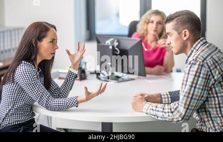 Donna gesticules ad un uomo arrabbiato per disaccordo con mediatore demale seduto dietro il tavolo sullo sfondo. Foto Stock