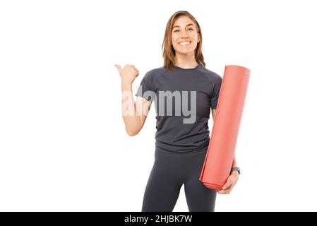 Foto della giovane donna sportiva che tiene il tappeto rosso yoga e punta via. Foto Stock