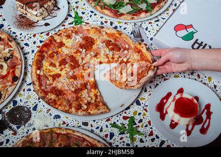 Una donna sta mangiando la pizza di peperoni dal forno a legna. Pranzo in un ristorante italiano. Foto Stock