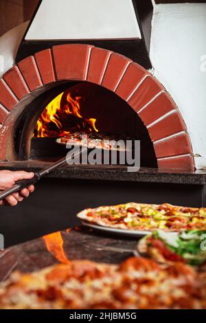 lo chef prende la pizza. La pizza italiana viene cotta in forno a legna Foto Stock