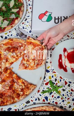 Una donna sta mangiando la pizza di peperoni dal forno a legna. Pranzo in un ristorante italiano. Immagine verticale Foto Stock