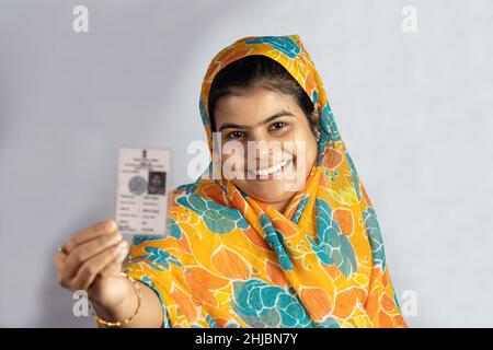 Una giovane donna indiana sorridente con la carta elettore in mano su sfondo bianco Foto Stock