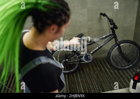 Da sopra di meccanico femminile con dreadlock lavaggio bicicletta con acqua da tubo. Sta lavorando in un servizio di riparazione Foto Stock