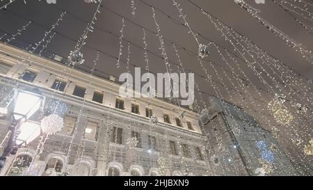 Belle ghirlande appese sulla strada della città. Azione. Vista dal basso delle scintillanti ghirlande che adornano la strada. Decorazioni festive di strade e case di Foto Stock