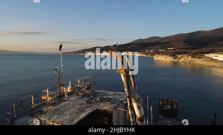 Vecchia barca in piedi sulla spiaggia al tramonto cielo sfondo. Scatto. Gabbiani seduti su una nave rotta al tramonto. Foto Stock