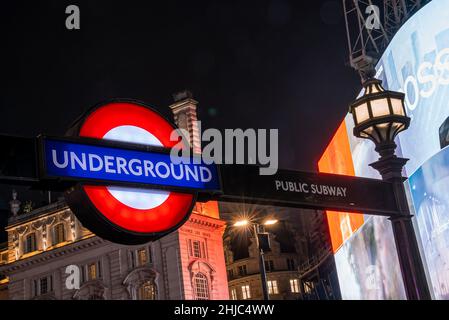Famoso cartello della metropolitana pubblico di Londra con luci di strada Foto Stock