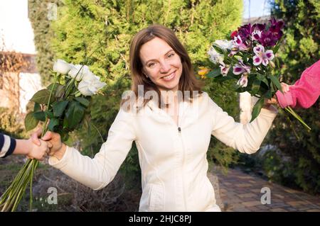 ritratto di una donna sorridente felice, alla quale le mani dei bambini tengono fuori due mazzi di fiori. Emozioni gioie, positive, maternità. Congratulazioni f Foto Stock