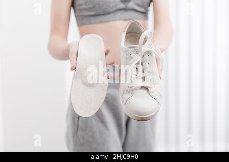 Donna fitness in abbigliamento sportivo con sottopiedi ortopedici e sneakers. Donna che mette la soletta ortopedica nella scarpa da vicino a casa. Striscione per la cura del piede. Piatto Foto Stock