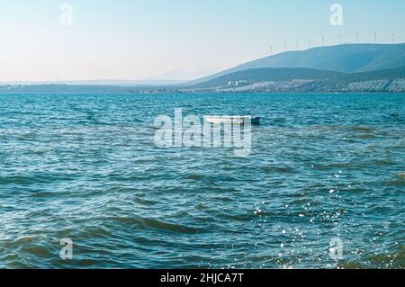 Barca nella baia nel villaggio di Akbuk in Turchia. Vista sulla baia e sulle colline. Turbine di un parco eolico sulle colline Foto Stock