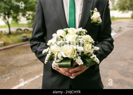 Un uomo tiene un bouquet di nozze nelle sue mani. Concetto di San Valentino. Il concetto di matrimonio. Sposarsi con un bouquet. Lo sposo in un vestito tiene un matrimonio Foto Stock