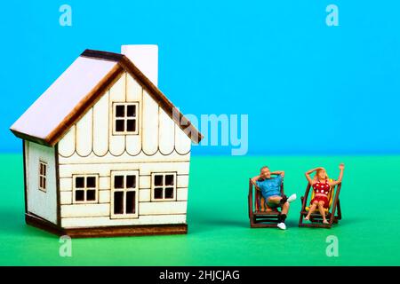 Immagine concettuale di una coppia di figure in miniatura sedette in sdraio a lato di una casa modello Foto Stock