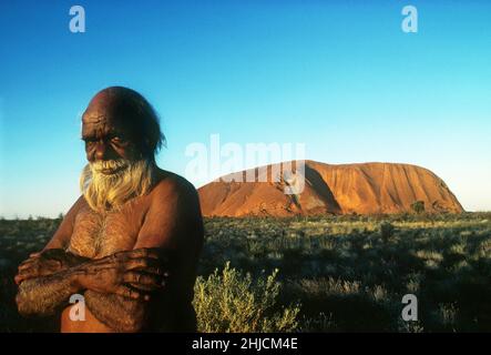 Toby Kaninga, un australiano indigeno, si trova vicino alla grande formazione di arenaria conosciuta come Ayers Rock. La pietra miliare è sacra per gli aborigeni della zona, a volte rendendo il turismo una questione delicata. Foto c.. 1982. Foto Stock