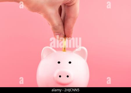 Rosa Piggy Bank e la mano di un uomo mette giù una moneta su uno sfondo rosa. Concetto di shopping di affari in linea Foto Stock