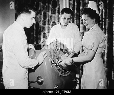 Un infermiere e due corpsmen assistono ad un paziente di poliomielite in un polmone di ferro. Esercito degli Stati Uniti, 1949. Foto Stock