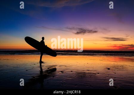 I surfisti su una spiaggia lucida con bassa marea guardano un colorato tramonto invernale dopo il surf a Torrey Pines, San Diego, California. Foto Stock