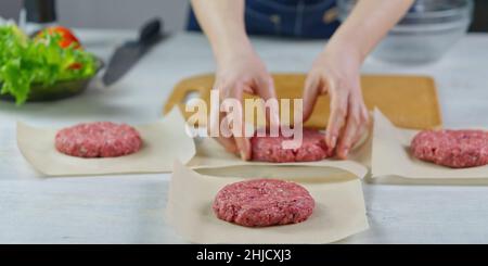 Mano della donna che forma una carne di manzo per una festa di hamburger. Porzionamento carne macinata. Hamburger fatti in casa. Fare il cibo a casa. Foto Stock