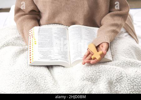 Un primo piano di una mano che tiene una croce di legno sopra la bibbia Foto Stock