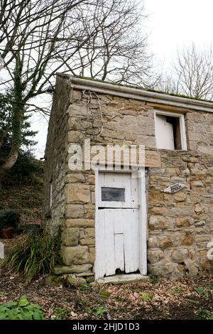 Un vecchio fienile in pietra vicino Aston, Derbyshire con porte di legno dipinte di bianco in uno stato di disriparazione. Foto Stock