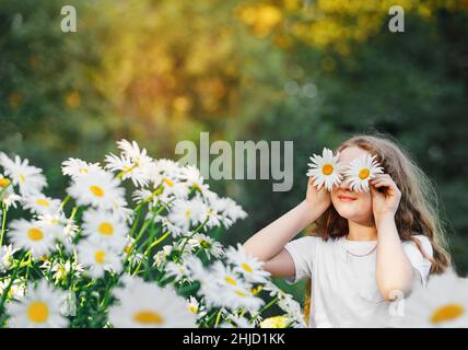 Bambino con occhi a margherita su sfondo verde in un parco estivo. Concetto di stile di vita sano. Foto Stock