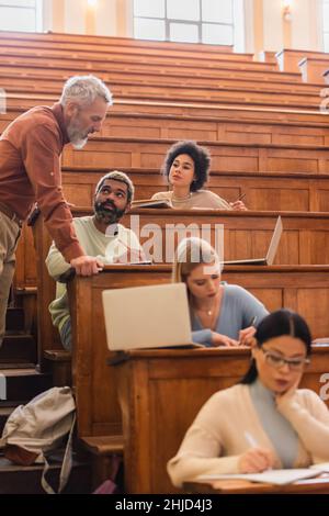 Gli studenti afroamericani guardano il professore mentre scrivono sui quaderni dell'università Foto Stock