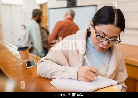 studente asiatico iscritto sul notebook vicino smartphone e caffè per andare in università Foto Stock