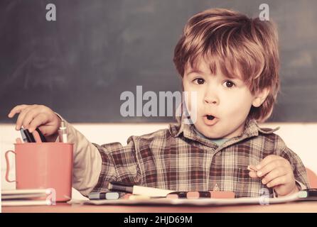 Preschooler vicino alla lavagna. Giovane studente. Istruzione e bambini. Un allievo sorridente che disegnava alla scrivania. Torna a scuola. Preschooler. Il bambino è Foto Stock