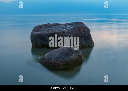 Ora blu dopo il tramonto sul mar Baltico roccioso costo. Piccole pietre e grandi massi in mare. Esposizione prolungata Foto Stock