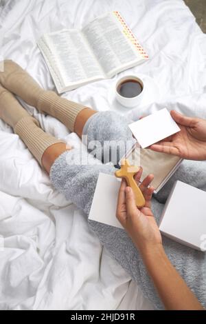 Un colpo verticale di una femmina che tiene una croce di legno, una scatola regalo e una carta con spazio per il testo Foto Stock