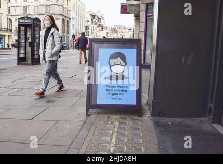 Londra, Regno Unito. 28th Jan 2022. Una donna che indossa una maschera per il viso come precauzione contro la diffusione del coronavirus cammina accanto a un cartello all'esterno di un negozio nel centro di Londra incoraggiando le persone a continuare a indossare maschere per il viso, se possibile, come l'Inghilterra finisce le coperture viso obbligatorie negli spazi pubblici interni. Credit: SOPA Images Limited/Alamy Live News Foto Stock