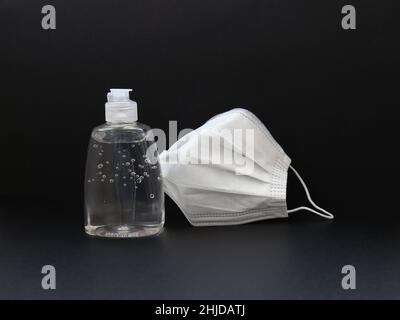 kit protettivo di base per pandemia covid19, gel igienizzante per le mani in flacone trasparente e maschera bianca in posizione verticale rispetto al flacone chiuso su sfondo nero Foto Stock