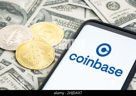 Galizia, Spagna; 28 gennaio 2022: Logo Coinbase sullo schermo dello smartphone e banconote in dollari e monete in bitcoin e etereo Foto Stock