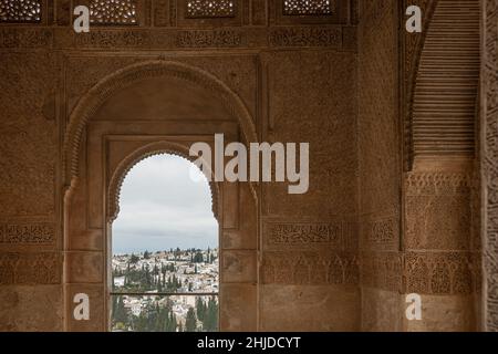 Dettagli decorati delle pareti interne del palazzo dell'Alhambra. Sullo sfondo, sotto l'arco, si possono ammirare le tipiche case bianche dell'Albaicin nei Foto Stock