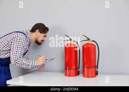 Un tecnico addetto alla sicurezza antincendio prende appunti durante il controllo degli estintori all'interno dell'edificio Foto Stock