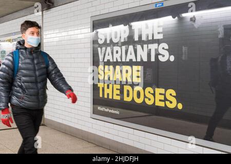 Un uomo in maschera di faccia cammina davanti enorme poster sul tabellone mostrando 'le varianti condividono le dosi', Londra Inghilterra Regno Unito Foto Stock