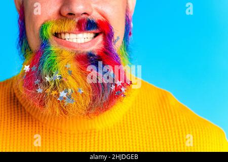 bell'uomo con raindow in barba con confetti glitter in baclground blu studio Foto Stock