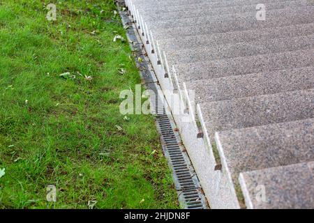 Sistema di drenaggio su un pendio con erba verde e sistema di precipitazioni in ferro vicino ad una scala di granito con gradini di pietra primo piano, nessuno. Foto Stock