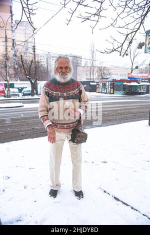 Ucraini. L'uomo anziano ucraino in un maglione in un gelido giorno di gennaio sta rimanendo sulla strada a Kiev, con un vetro di plastica della lager nella mano sinistra. Foto Stock