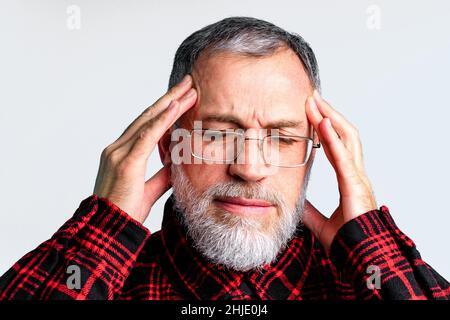 Ritratto di uomo maturo isolato su sfondo grigio che soffre di grave mal di testa, chiudere gli occhi per alleviare il dolore Foto Stock