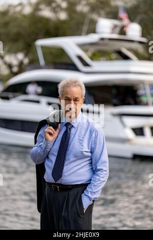 Uomo d'affari riuscito che posa con uno yacht di lusso sfocato nello sfondo Foto Stock