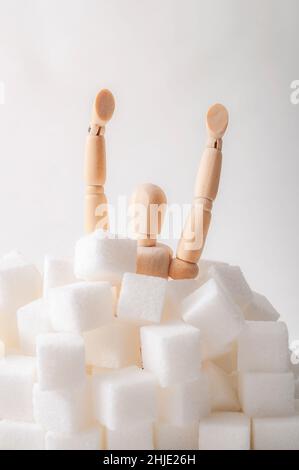Dipendenza da zucchero, resistenza all'insulina, dieta malsana e novembre 14 è il concetto di giornata di sensibilizzazione al diabete con un burattino che annegava in cubetti di zucchero isolati o Foto Stock