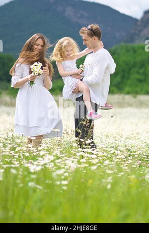 Famiglia felice sul grande prato di montagna camomilla. Scena emozionale, d'amore e di cura. Foto Stock