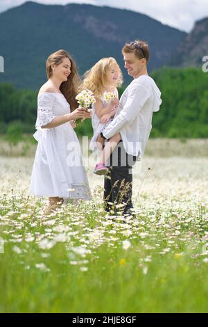 Famiglia felice sul grande prato di montagna camomilla. Scena emozionale, d'amore e di cura. Foto Stock
