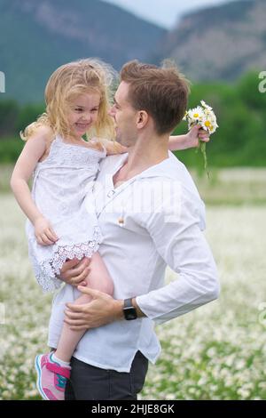 Felice padre e figlia in grande camomilla prato di montagna. Scena emozionale, d'amore e di cura. Foto Stock