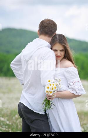 Coppia felice sul grande prato di montagna camomilla. Scena emozionale, d'amore e di cura. Foto Stock